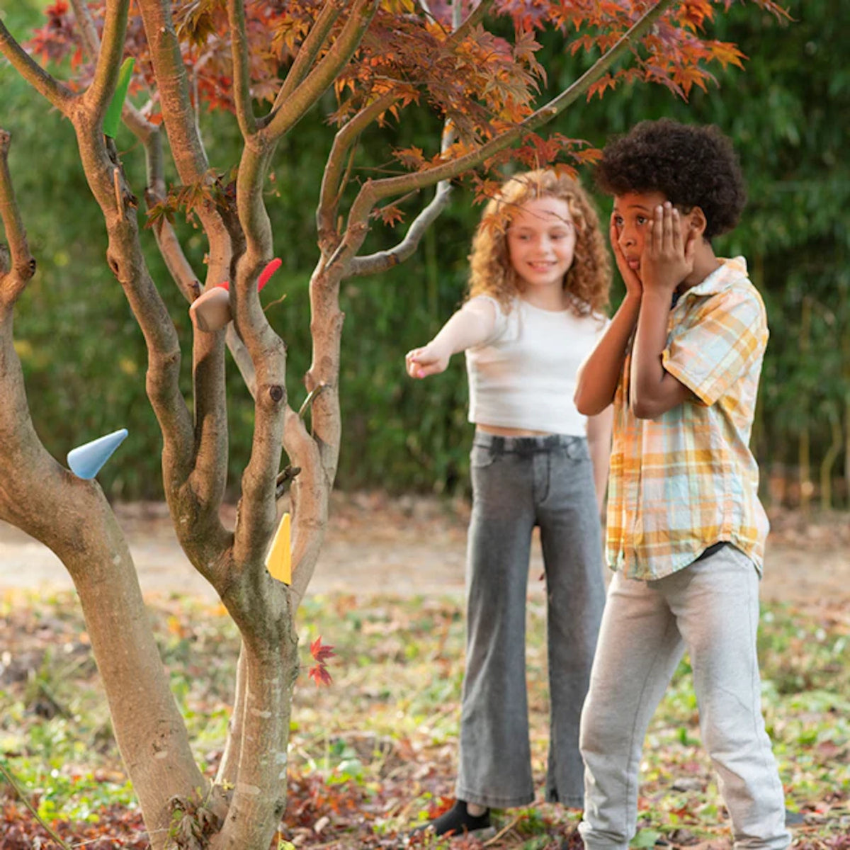 Two kids playing a hide and seek game called Where Is My Hat outdoors by a tree.