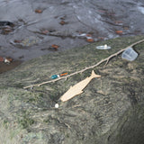 A wooden fish-shaped hand reel and fishing line with a bobber rest on a rock by a stream.