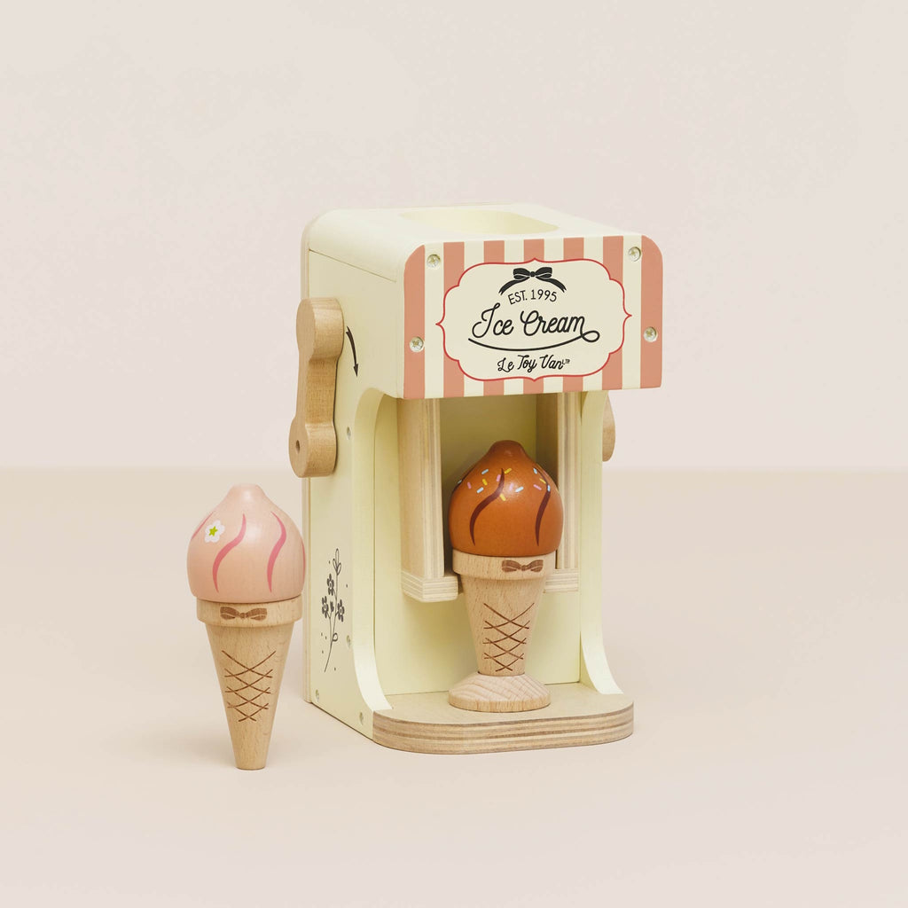 Wooden toy ice cream machine with a pink and white striped design. It features a cone with a scoop on top and an ice cream cone in the opening below.
