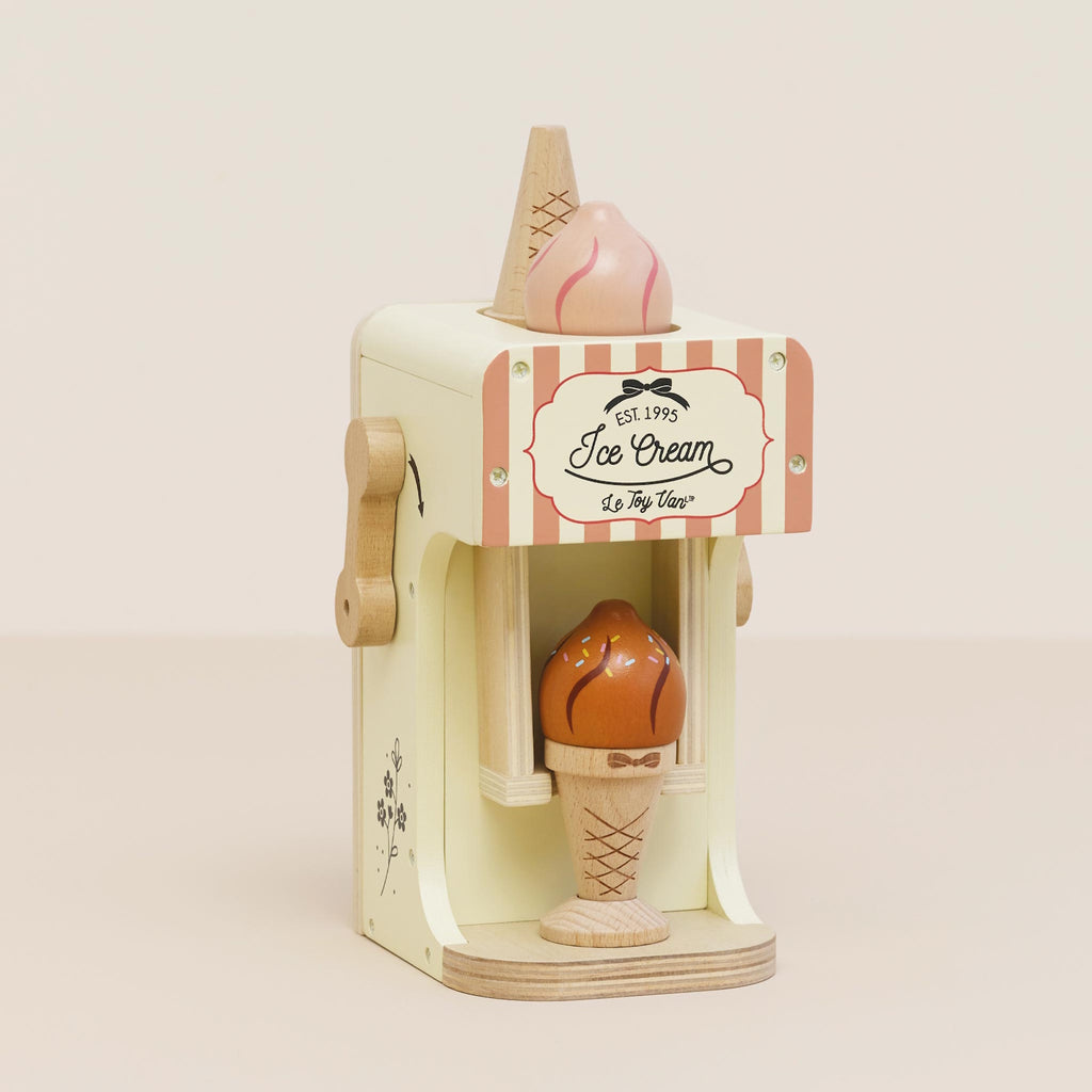Wooden toy ice cream machine with a pink and white striped design. It features a cone with a scoop on top and an ice cream cone in the opening below.