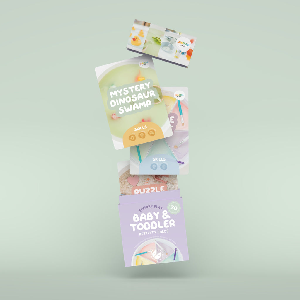 Box of "Baby & Toddler Activity Cards" for sensory play. Features playful design, pastel colors, rubber duck, paint, and crafting materials.