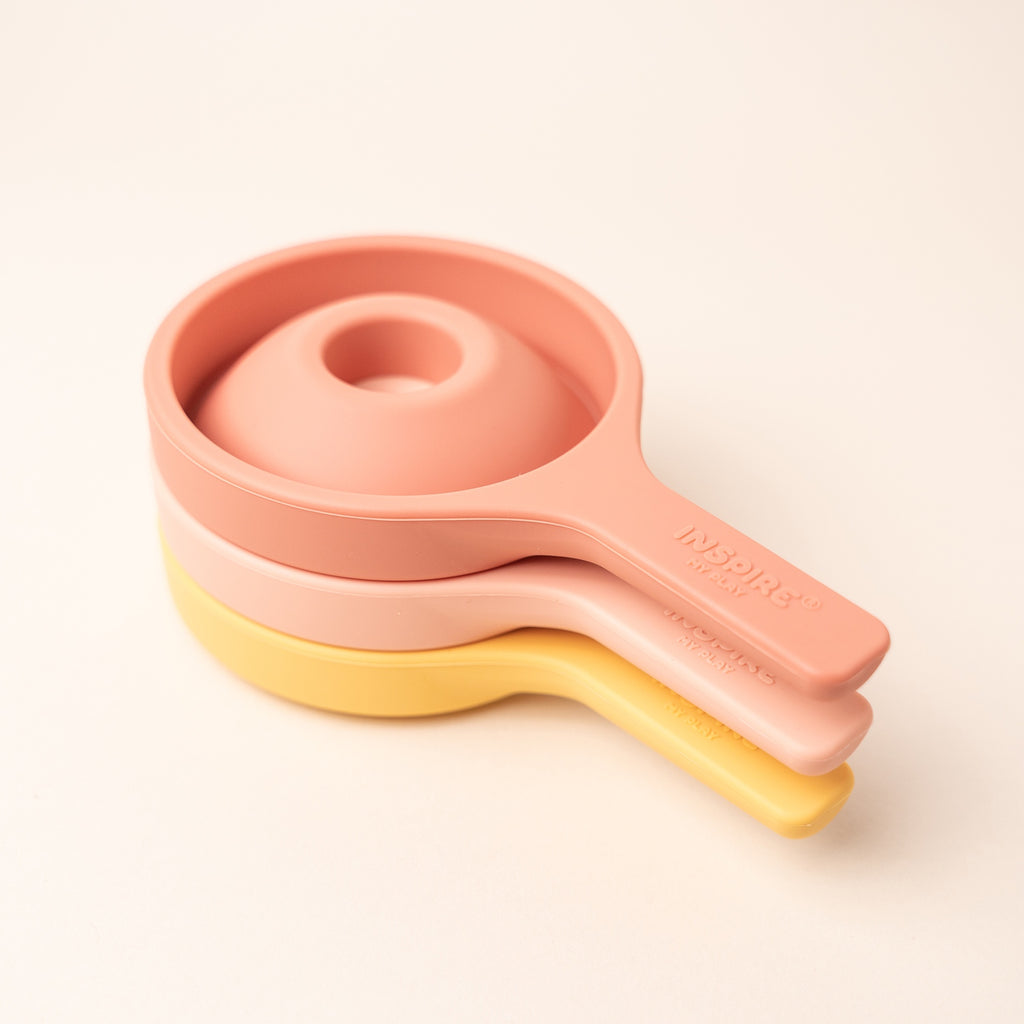 Three nested silicone funnels in pastel colors coral and yellow, stacked vertically. They convey a neat, organized kitchen accessory setup.