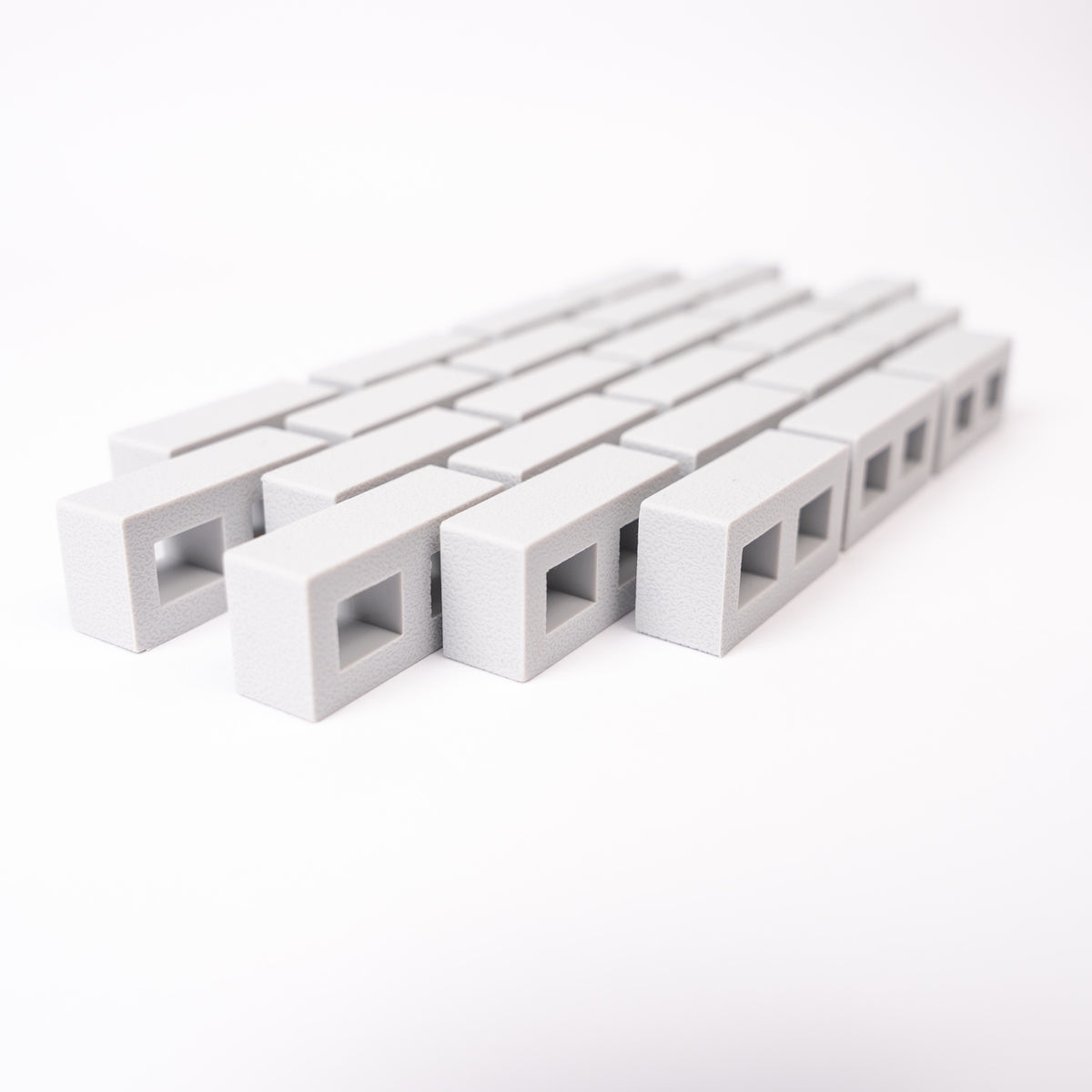 A close-up of rows of small, rectangular, gray blocks with square openings, aligned diagonally on a white background, creating a minimalistic pattern.