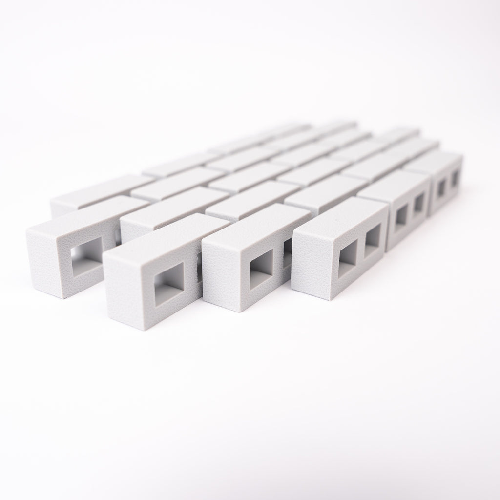 A close-up of rows of small, rectangular, gray blocks with square openings, aligned diagonally on a white background, creating a minimalistic pattern.