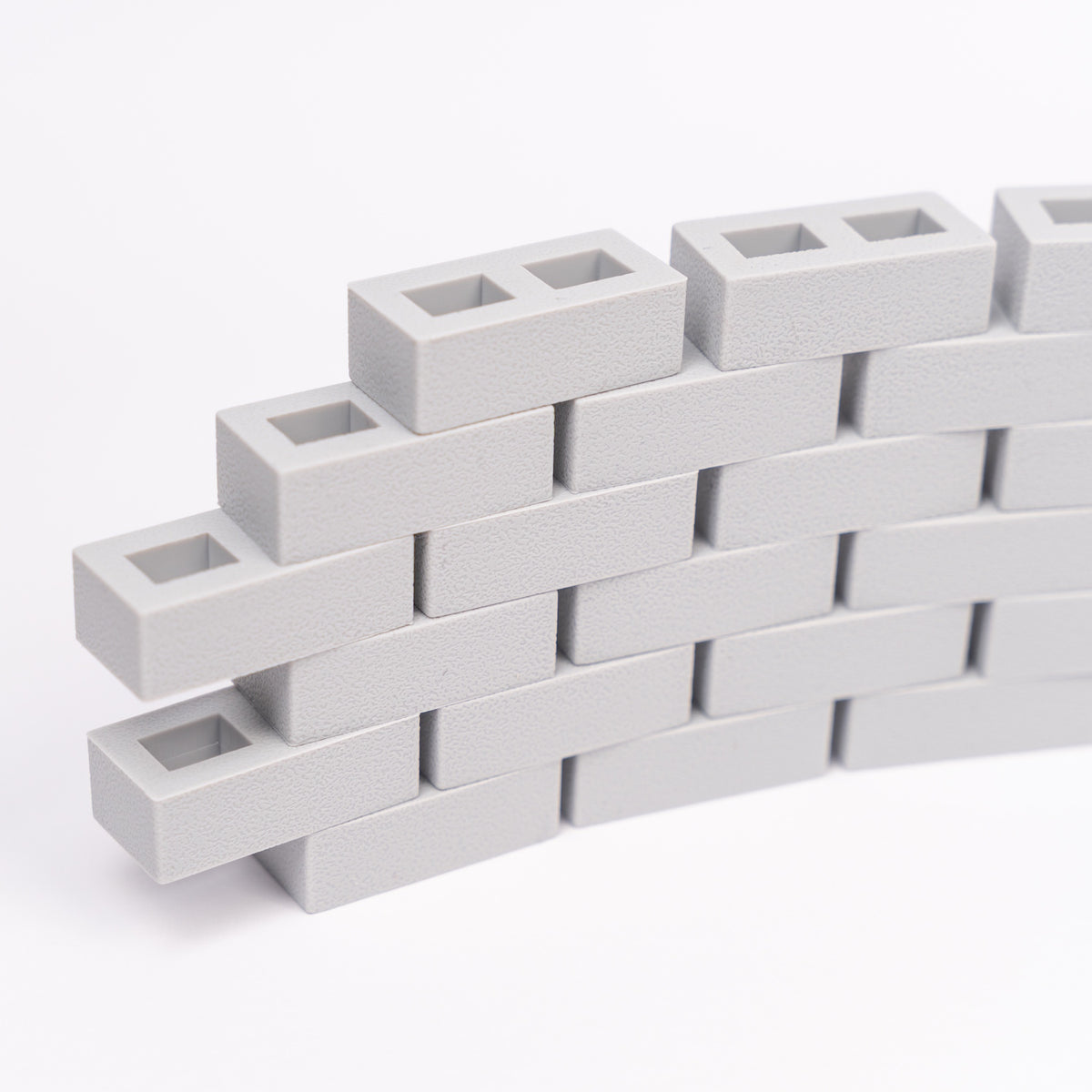 Stacked light gray interlocking rectangle blocks form a small curved wall on a white background. The textured surface creates a modern, minimalist look.