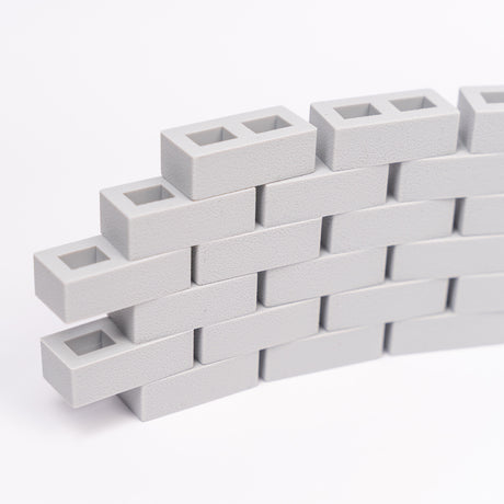 Stacked light gray interlocking rectangle blocks form a small curved wall on a white background. The textured surface creates a modern, minimalist look.