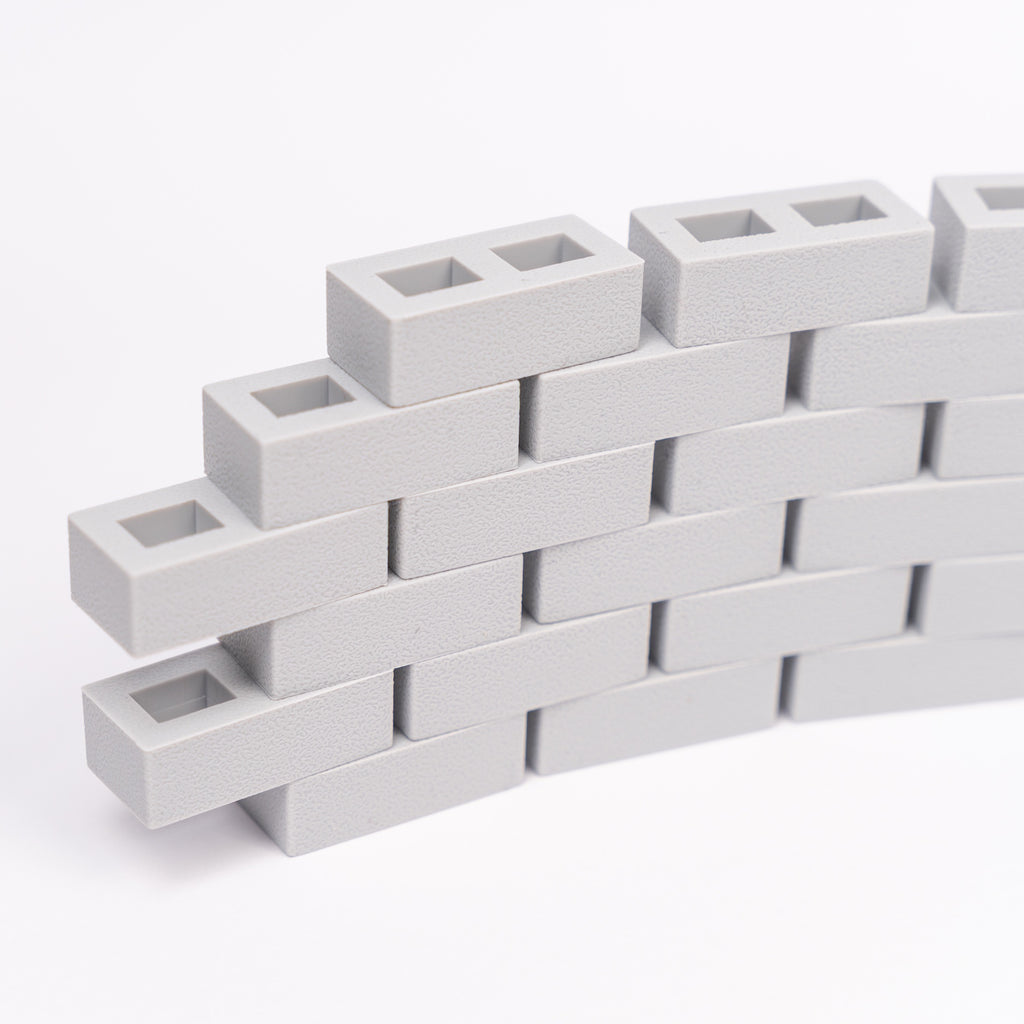 Stacked light gray interlocking rectangle blocks form a small curved wall on a white background. The textured surface creates a modern, minimalist look.