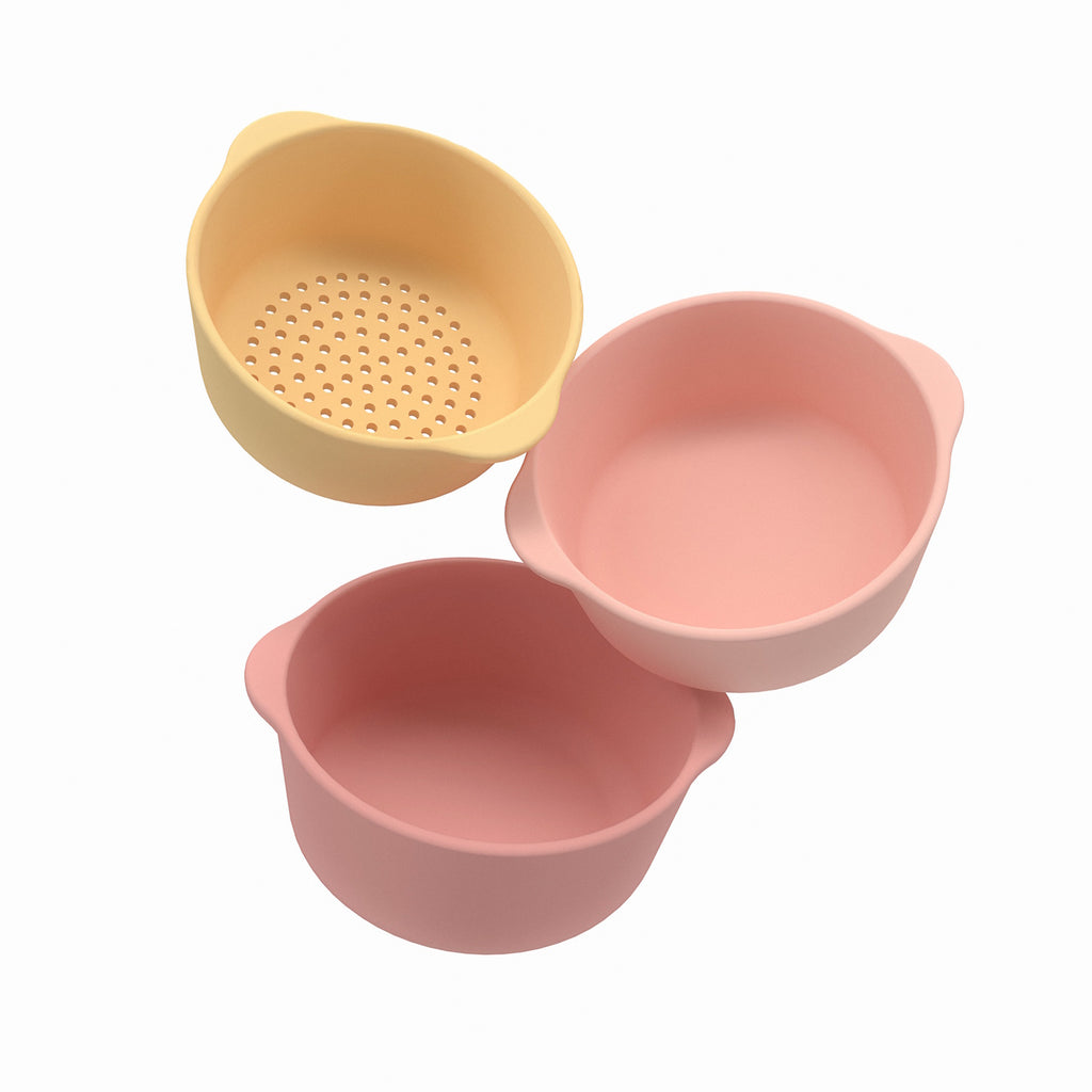 Three pastel silicone bowls; one yellow with holes as a colander, two solid pink, nested together. Minimalist design on a white background.