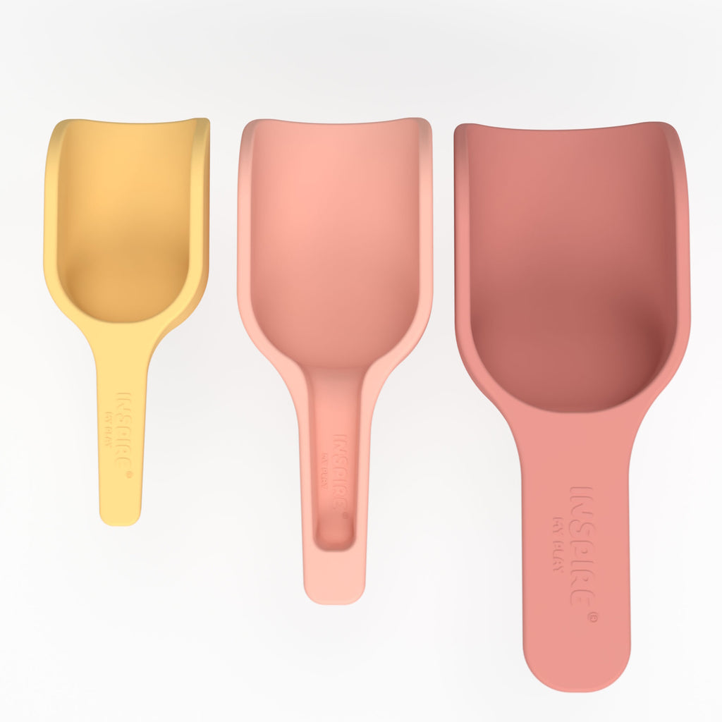 Three scoops in pastel colors—yellow, peach, and pink—are lined up in a row on a white background. They vary in size, conveying a playful tone.