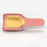 Stacked measuring cups in soft pink and yellow, featuring curved handles and a smooth finish. They convey a playful, modern kitchen aesthetic.