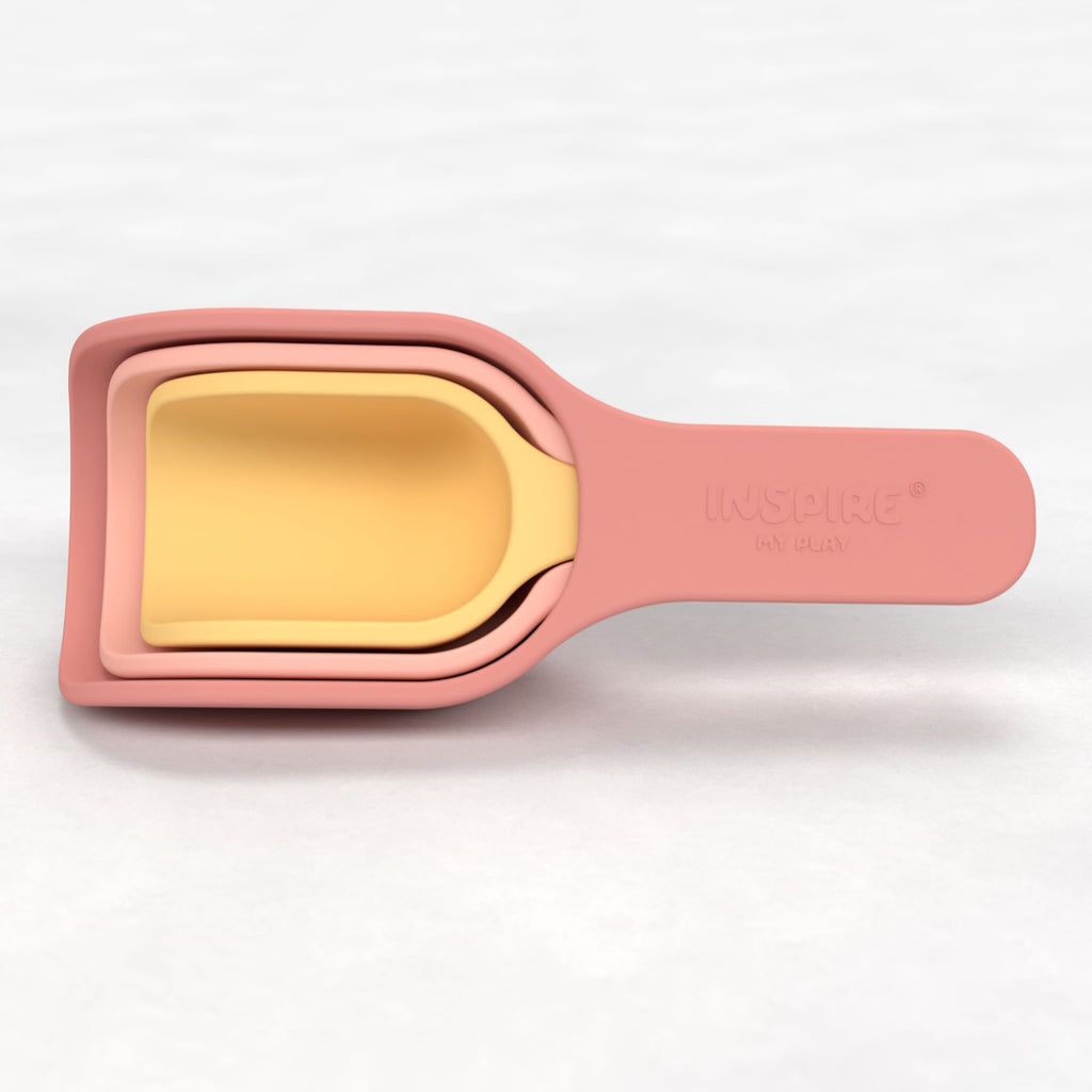 Stacked measuring cups in soft pink and yellow, featuring curved handles and a smooth finish. They convey a playful, modern kitchen aesthetic.