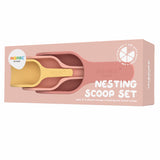 Packaging of a "Nesting Scoop Set" with three nested silicone scoops in muted pink and yellow. The box is blush pink, creating a calm, playful tone.