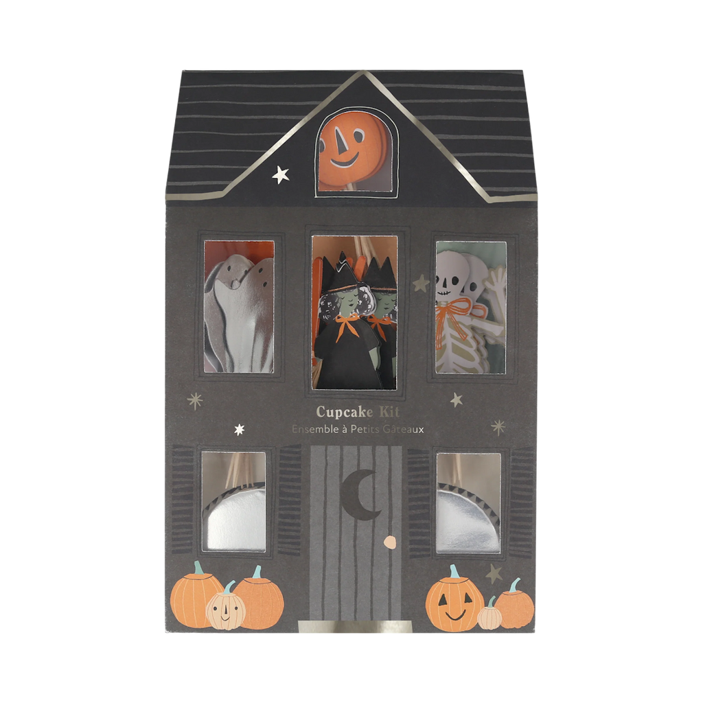 Halloween-themed cupcake kit packaging shaped like a haunted house. Features ghost, witch, and skeleton illustrations, with pumpkins and stars decorating the front. Spooky and festive atmosphere.