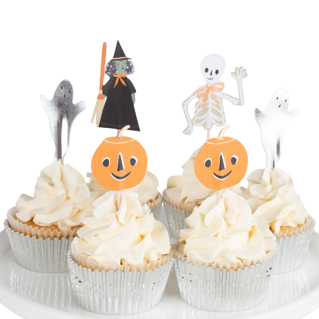 Four cupcakes with creamy frosting are topped with Halloween decorations: a witch, skeleton, ghosts, and pumpkins. Festive and playful atmosphere.