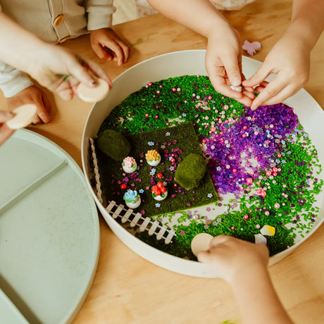 Children playing with a fairy garden sensory tray filled with green rice, purple crystals, and miniature decor.