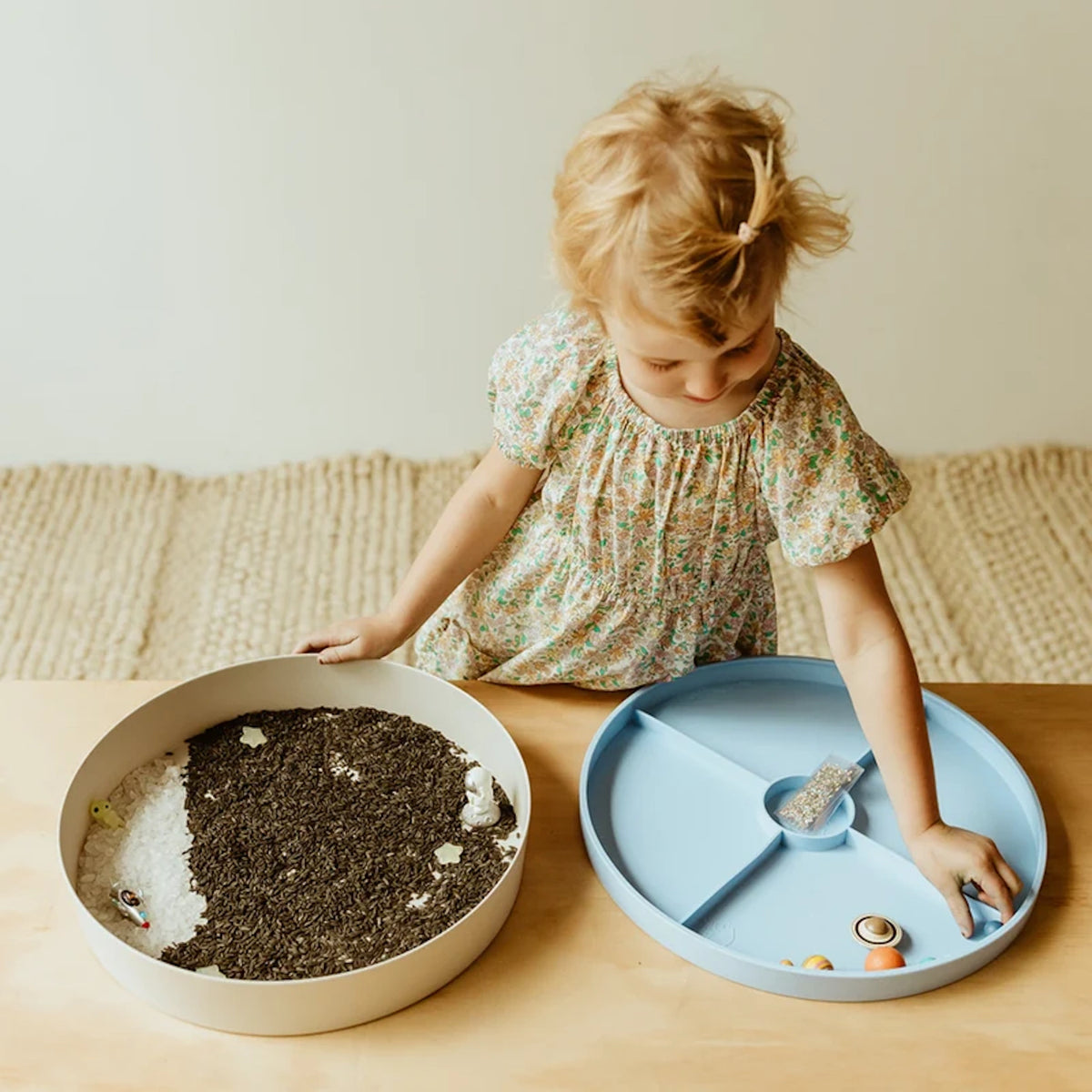 A toddler playing with a galaxy sensory kit using round sorting trays filled with rice, stars, and planets.
