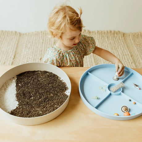 Toddler playing with a Jellystone Designs galaxy sensory kit filled with space toys and rice.