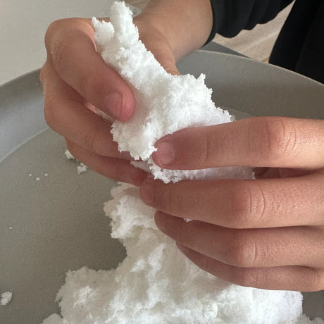 Hands shaping fluffy white Jellystone Designs sensory snow over a play tray.