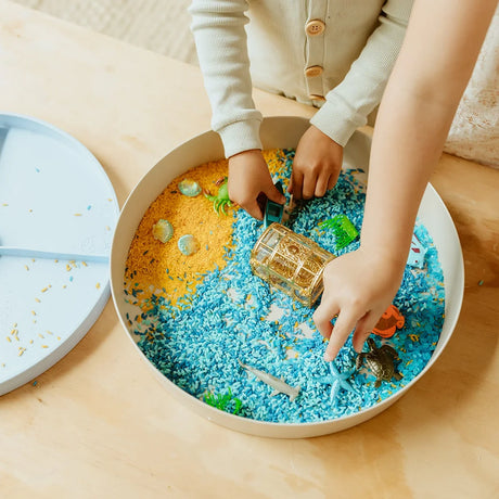 Child playing with Jellystone Designs Under The Sea sensory tray containing colored rice, sea creatures, and a treasure chest.