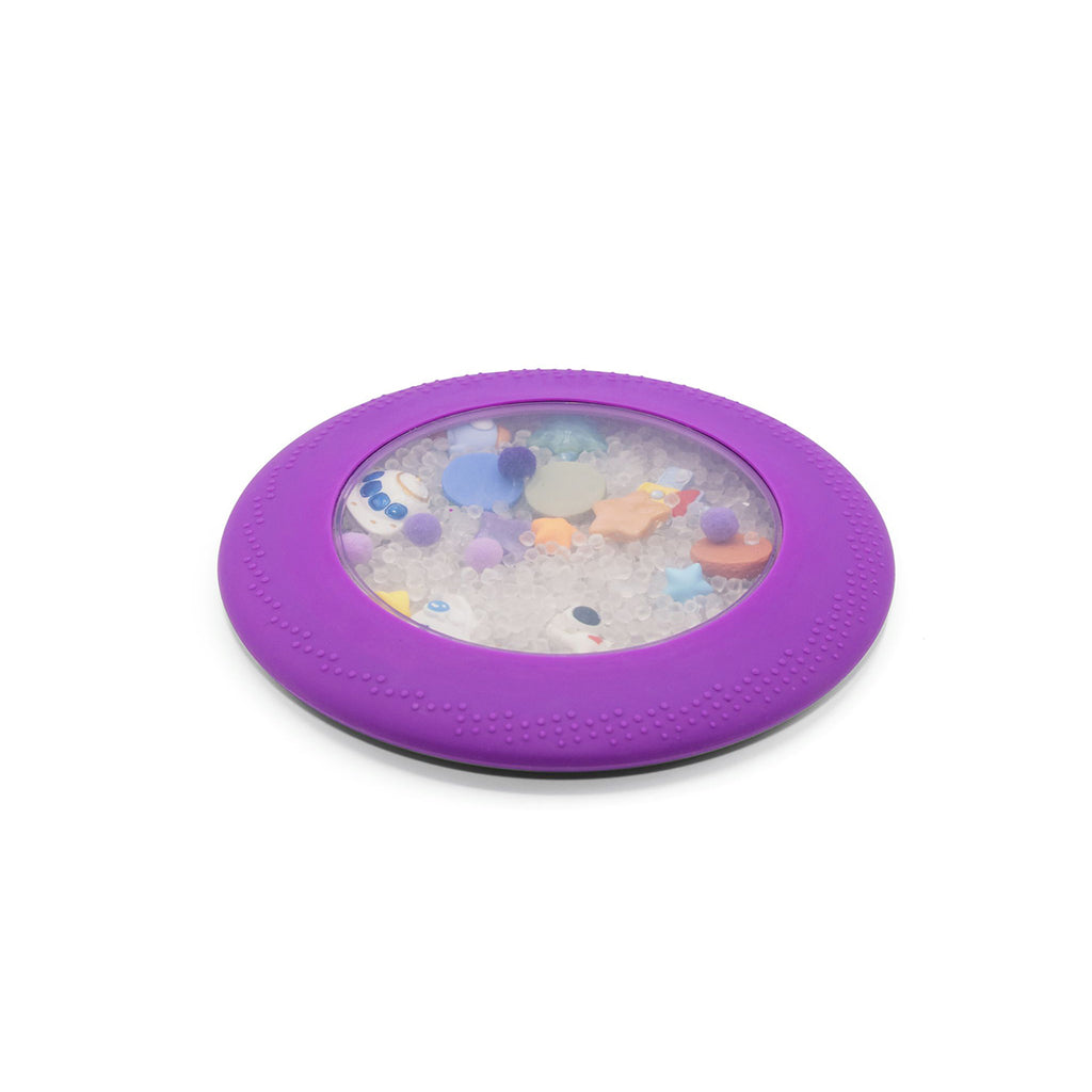 A purple Jellystone Peekaboo Bag filled with small sensory beads and space-themed charms inside a soft, circular frame.