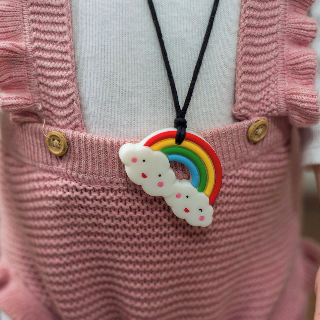 A close-up of a child wearing the rainbow and cloud silicone pendant necklace over a pink knitted outfit.