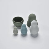 Four silicone nesting dolls in muted grey and blue tones shown partially unnested in a flat lay view.