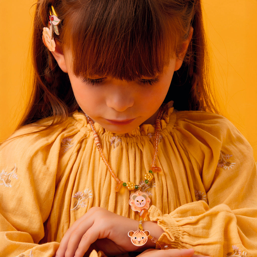 Young girl in a yellow dress looks down, displaying a matching animal-themed necklace and bracelet. The bright yellow background enhances a warm, cheerful tone.