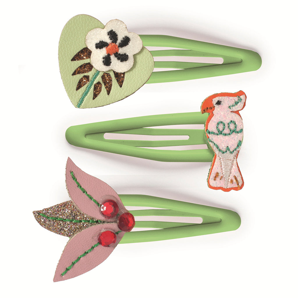 Three green hair clips adorned with playful designs: a flower on a heart, a colorful bird, and glittery leaves with red gems, conveying a fun and whimsical vibe.