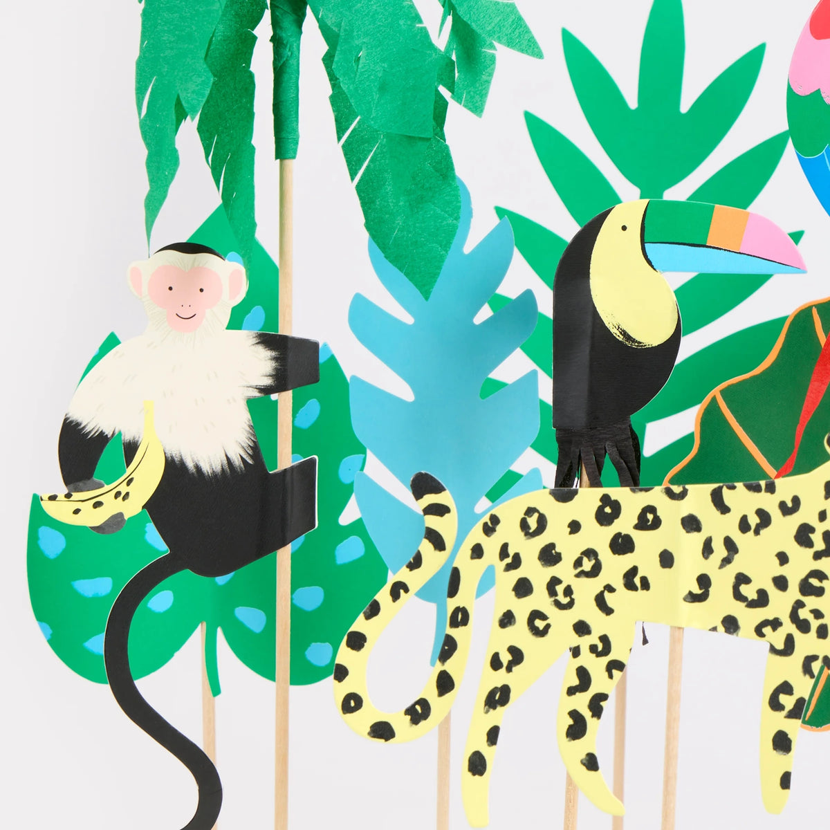 Paper-cut jungle animal cake toppers, including a monkey, toucan, and leopard, with tropical leaf decorations.