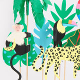 Paper-cut jungle animal cake toppers, including a monkey, toucan, and leopard, with tropical leaf decorations.