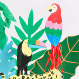 Close-up of vibrant jungle-themed paper cake toppers featuring a toucan, parrot, cheetah, and tropical leaves.