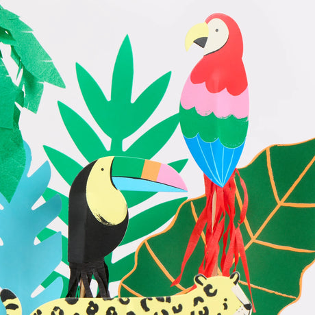 Close-up of vibrant jungle-themed paper cake toppers featuring a toucan, parrot, cheetah, and tropical leaves.
