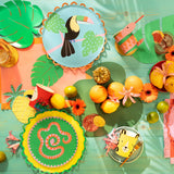 Jungle-themed party table with animal plates, colorful cups, tropical leaves, and fresh citrus fruits.