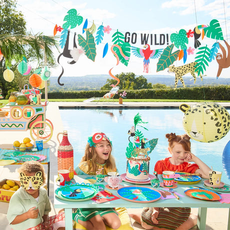 Three children enjoy a jungle-themed pool party with vibrant decorations, animal masks, and a colorful cake.