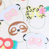 Colorful paper animal masks (cheetah, sloth, monkeys, and parrot) with green elastic strings on a white surface.