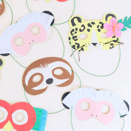 Colorful paper animal masks (cheetah, sloth, monkeys, and parrot) with green elastic strings on a white surface.