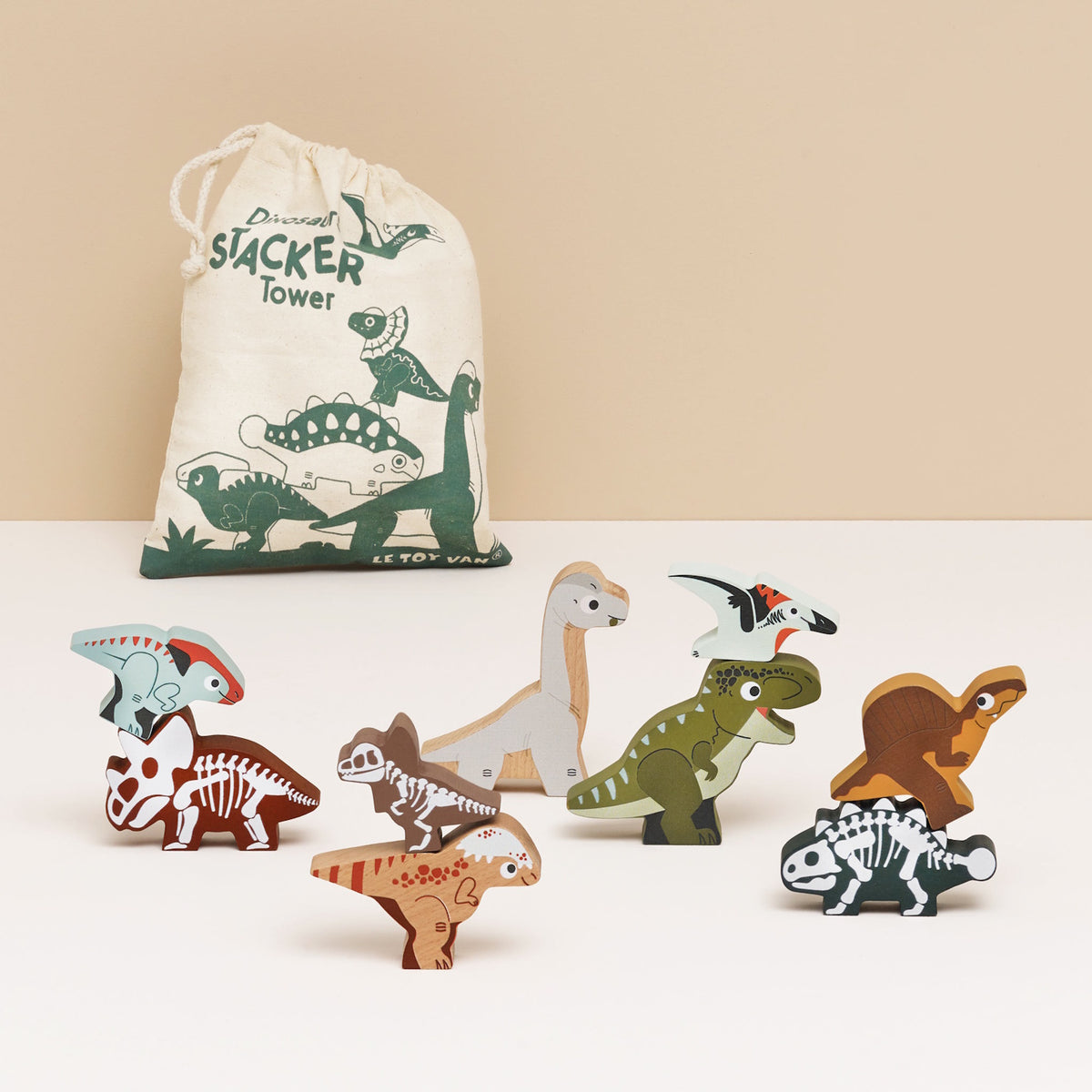 Wooden dinosaur figures stacked in pairs, set in front of a printed drawstring cotton bag.