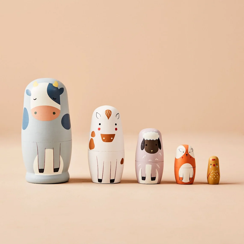 Five nesting dolls resembling cute animals, including a cow, horse, sheep, fox, and chick, are arranged from largest to smallest on a beige background.