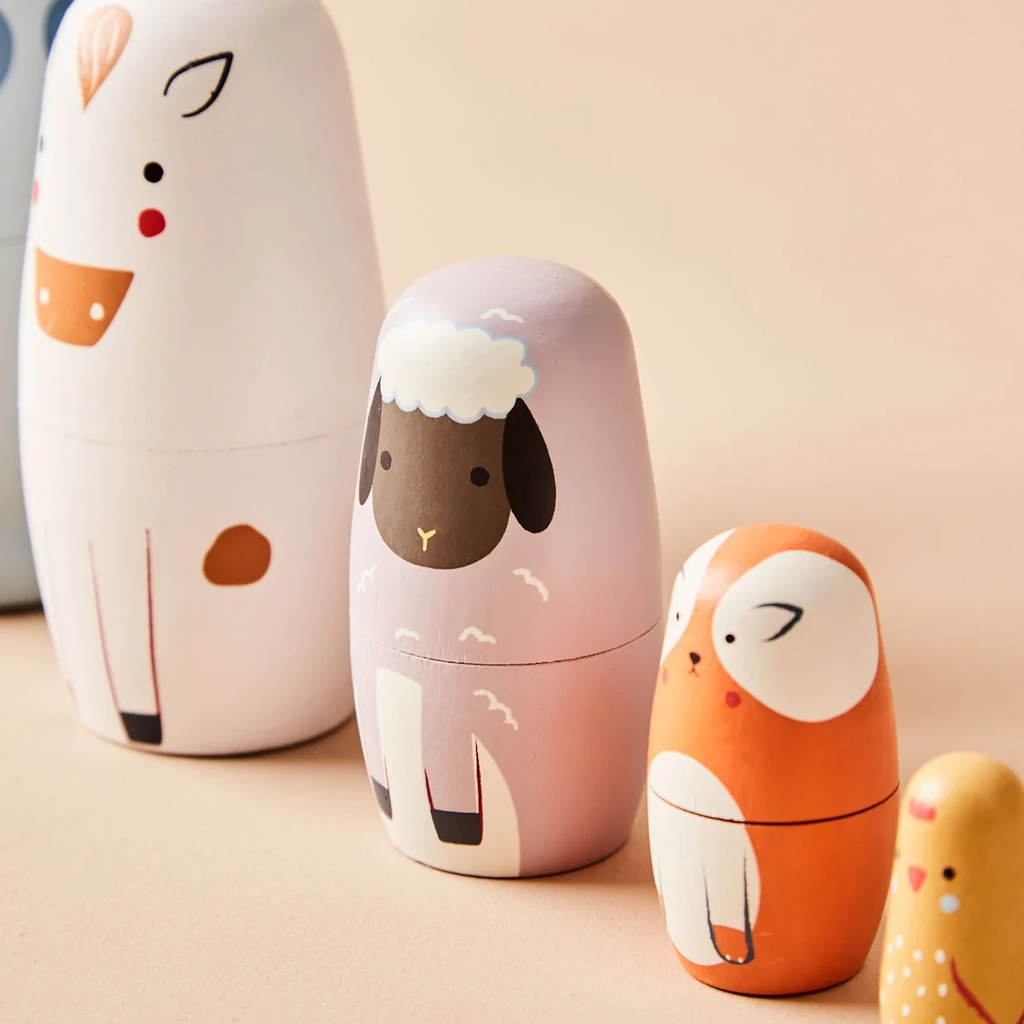 Cute, colorful nesting dolls resembling animals, including a white horse, pink sheep, orange dog, and yellow chick, arranged on a beige background.