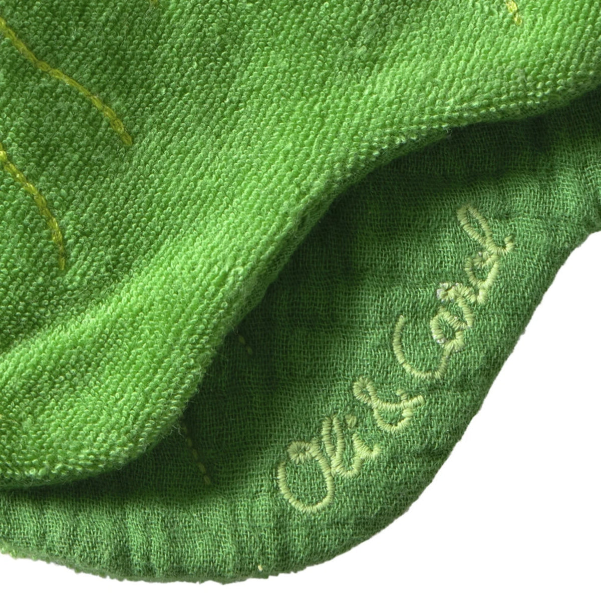 Close-up of a green muslin kale baby bib by Oli & Carol, showing embroidered brand logo and soft textured fabric.