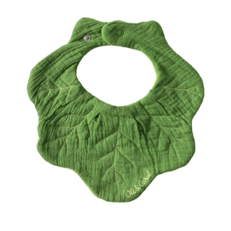 Green kale leaf-shaped muslin baby bib with stitched vein details and a snap closure, featuring the Oli & Carol logo.