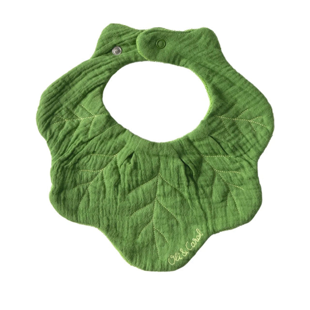 Green kale leaf-shaped muslin baby bib with stitched vein details and a snap closure, featuring the Oli & Carol logo.