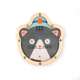 Wooden cat-shaped toy with a gray cat face wearing a blue hat with an orange flower. Its playful expression is framed by a light wood border.