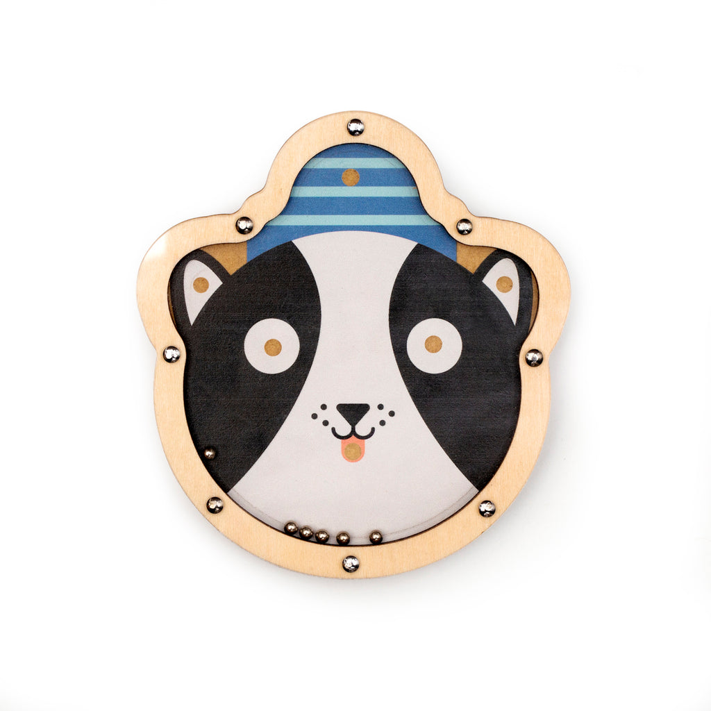 Wooden toy with a cartoon dog's face, featuring large eyes and a smiling mouth. It's outlined with metallic studs and includes small metal balls.