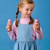 A young girl in denim overalls and a pink shirt holds two pink ice cream jump rope handles against a blue background with a smiling sun decoration.
