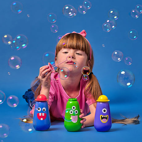 A girl in a pink shirt and headband joyfully blows bubbles. Colorful bottles with cartoon faces surround her against a bright blue background.