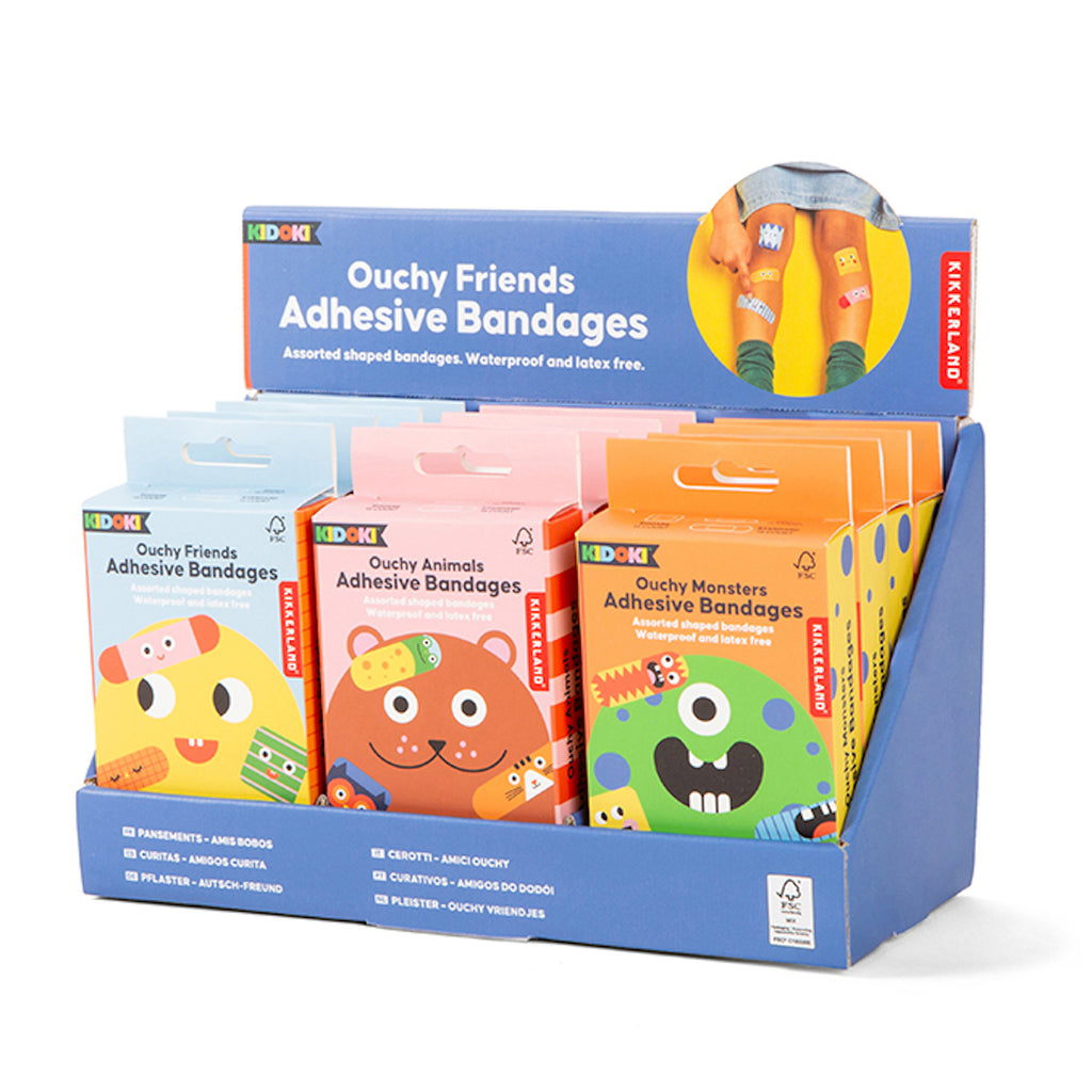 Display box with three packs of Kikkerland adhesive bandages: "Ouchy Friends" in blue, "Ouchy Animals" in pink, and "Ouchy Monsters" in orange. Fun and colorful.