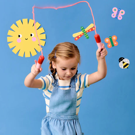 Young girl playing with Kidoki Popsicle Skipping Rope with colorful cartoon stickers on blue background.
