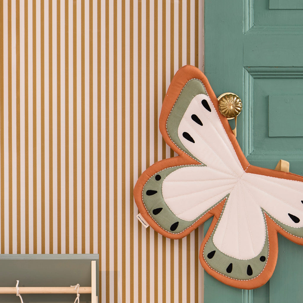 Fabric butterfly wings costume in soft orange, cream, and sage green with black teardrop accents. Two yellow straps suggest they can be worn. Bright and whimsical design.