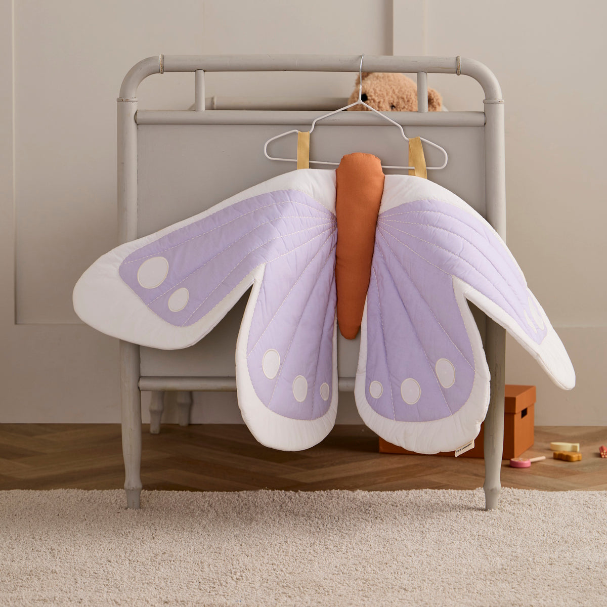 Soft fabric purple butterfly wings hanging on a white wire hanger attached to a crib.